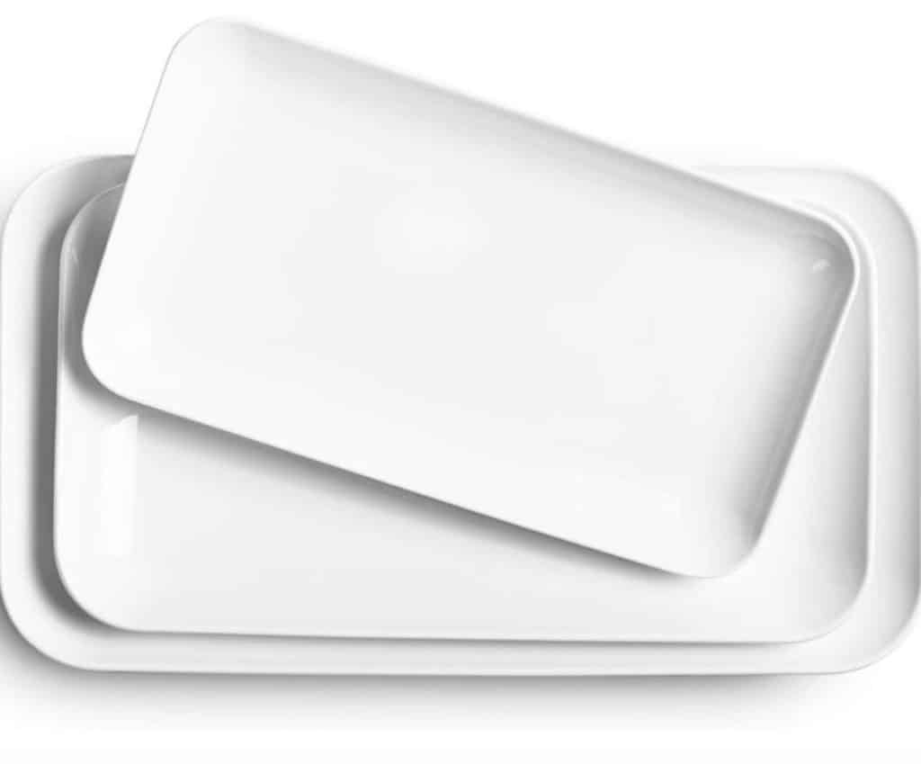 Two white rectangular ceramic trays are stacked, with the smaller tray placed slightly askew atop the larger one. Their smooth surfaces and rounded edges offer a minimalist elegance, perfect for serving your favorite infused chicken recipe with style.